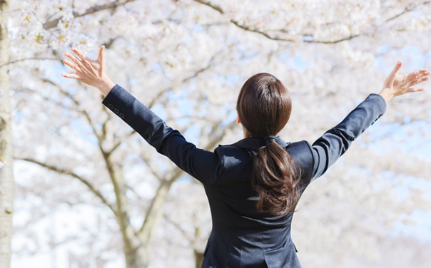 桜に向かって両手を広げるスーツの女性